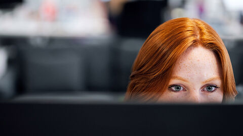 Quereinstieg in die Welt der IT – das Trainee-Programm der HZD  Frontalansicht von rothaariger junger Frau, die konzentriert auf einen Computermonitor schaut
