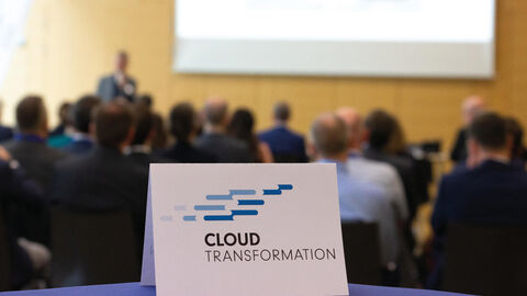 Gemeinsam in eine sichere Cloud: Kundenforum der HZD zu ihrem Programm Cloud-Transformation  Blick in den Veranstaltungsraum des Kundenforums Programm Cloud-Transformation der HZD mit Aufsteller des Programmlogos im Vordergrund