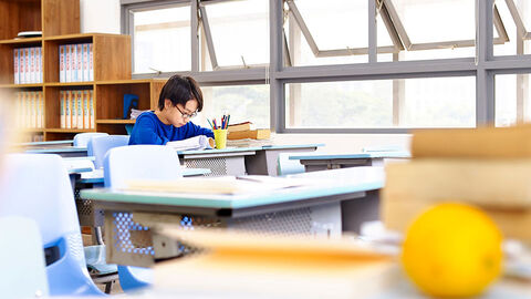Blick in ein modernes Klassenzimmer, wo ein einziger Schüler an seinem Tisch sitzt und arbeitet