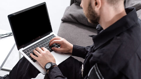 Ermittlungsergebnisse können nun auch digital von Polizei an Justiz übermittelt werden. Sitzender Beamter mit dunkler Uniform  und Laptop auf dem Schoß