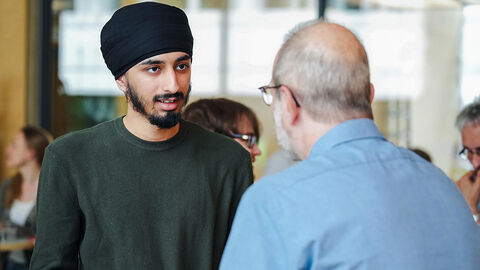 Ein junger Mann mit Migrationsgeschichte und Turban im Gespräch mit einem älteren Mann