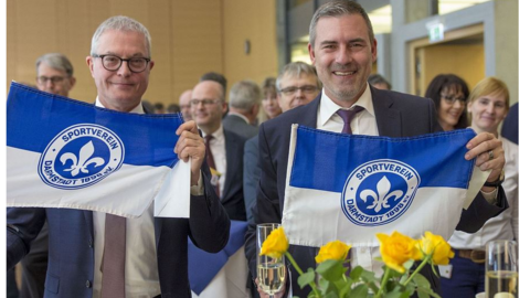 Doppelgeburtstag Joachim Kaiser und Thomas Kaspar Zwei Männer lachen in Kamera und halten Fahnen vom Sportverein Darmstadt in Kamera